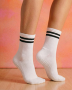 White non-slip pilates grips socks with black stripes worn by a person on a pink and orange gradient background