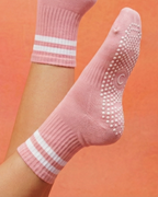 Pink rose pilates yoga grip socks with white stripes on a person's feet against an orange background