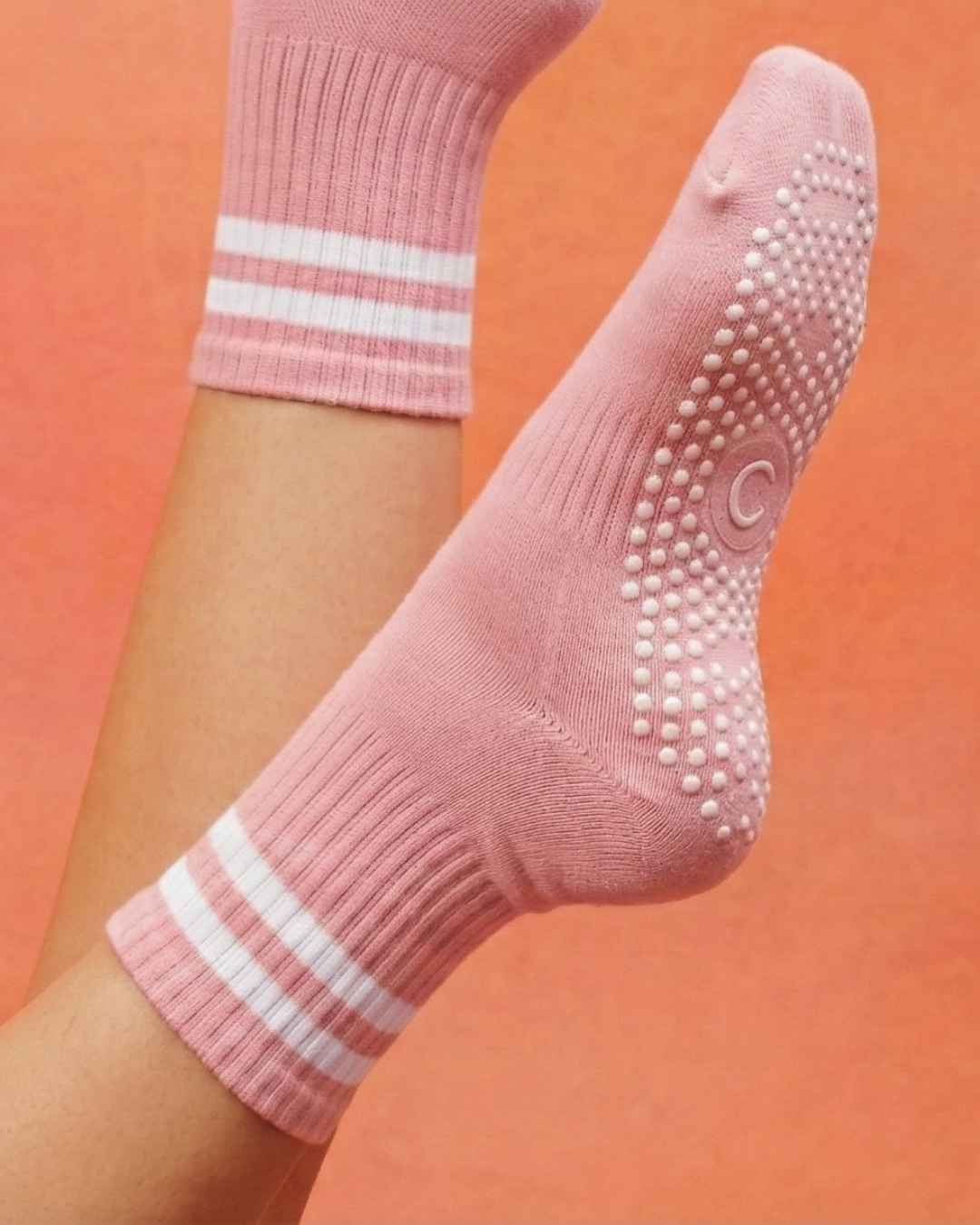 Pink rose pilates yoga grip socks with white stripes on a person's feet against an orange background